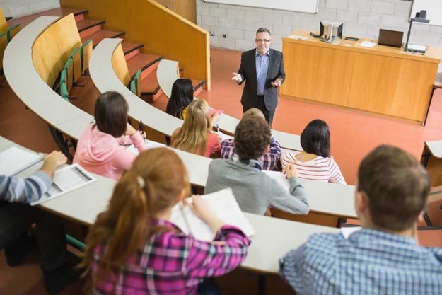 students take notes in a classroom while the male teacher alum finds passion in teaching