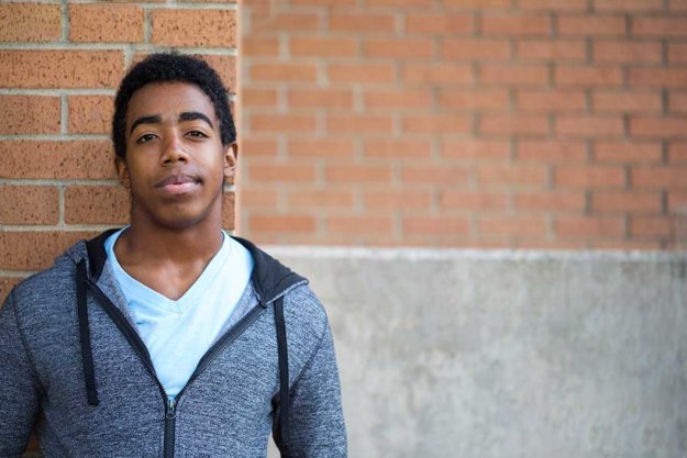 a teen leans against a brick wall and smiles because he's saying bye bye boot camp