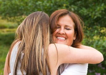 a mom smiles as she hugs her teen since they went over the bridge over troubled water