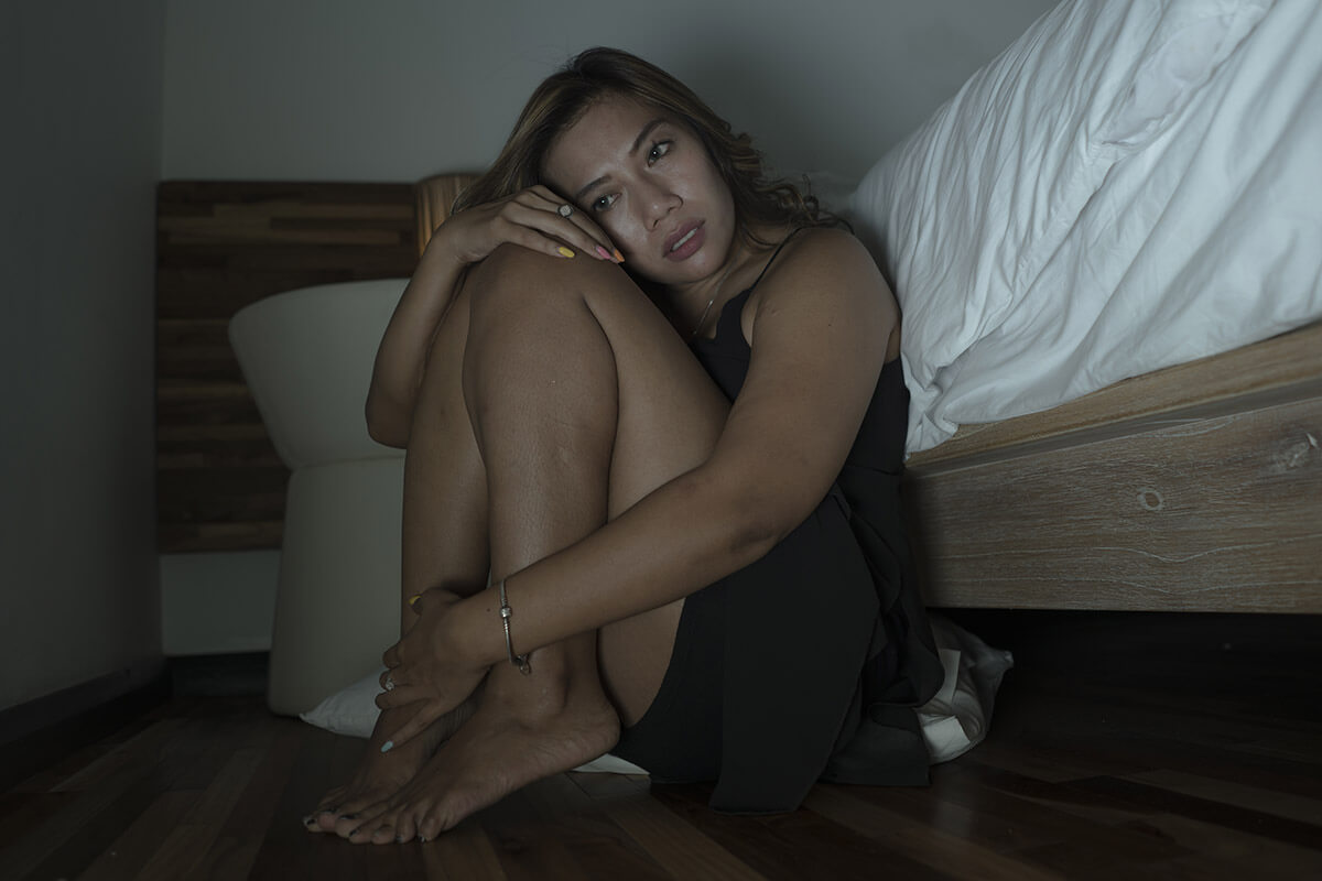 girl in dark sitting next to bed showing signs of mental illness