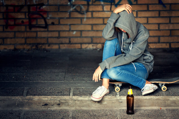 teen in hood sitting on curb drinking showing teen alcohol stats