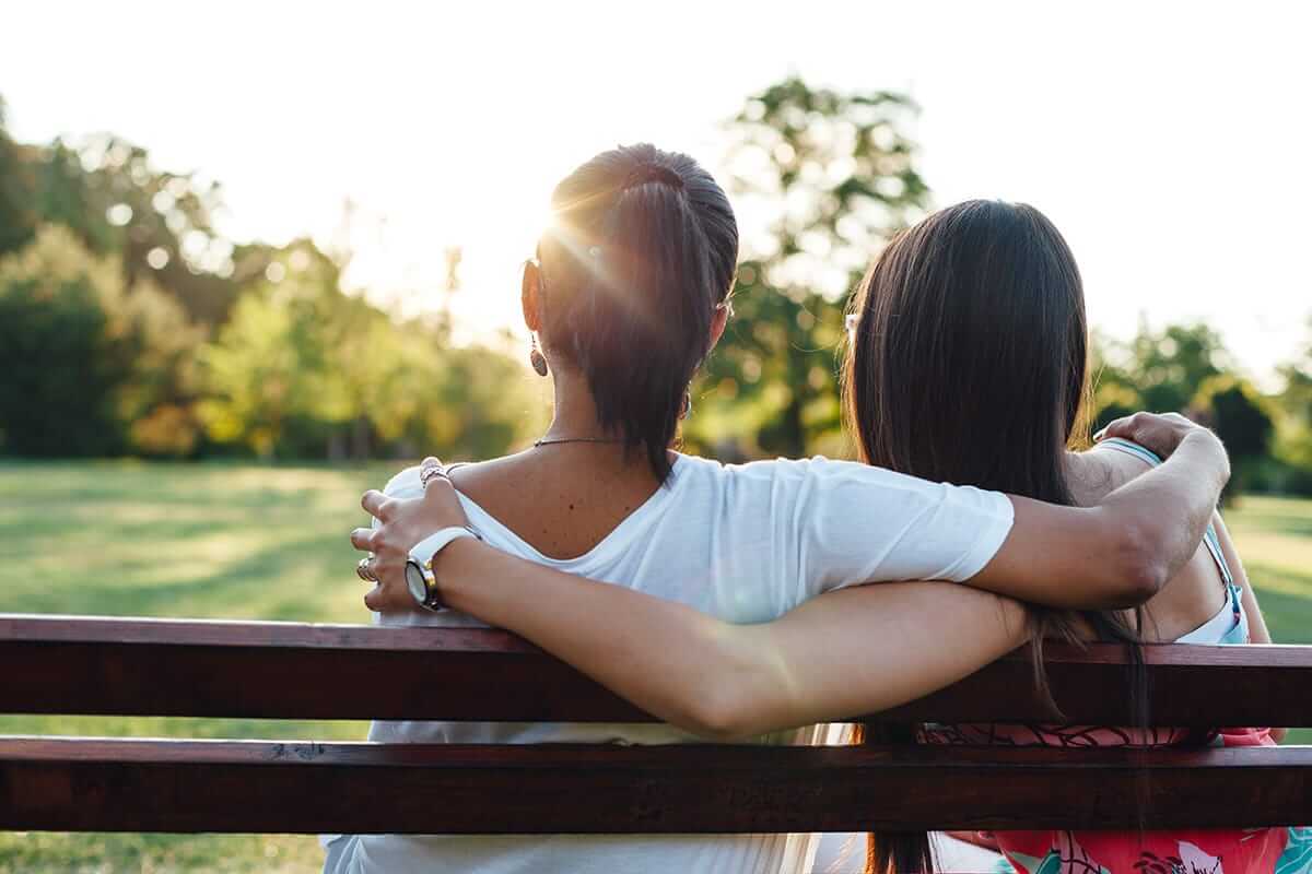 teen girls sit on a bench in nature with their arms around each other after learning how to improve mental health