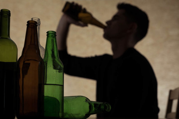 man drinking and surrounded by bottles ready to learn how to stop binge drinking