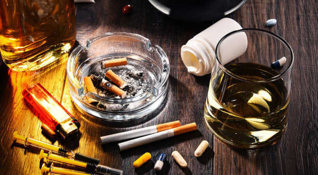 table shows alcohol, pills, a spilling pill bottle, cigarettes, a lighter and syringes for a user with polysubstance abuse