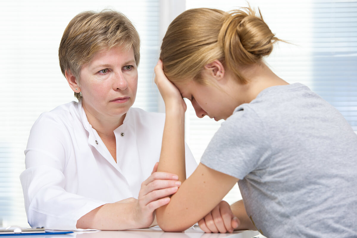 concerned female therapist talks to young distressed female about the symptoms of ptsd in teenagers