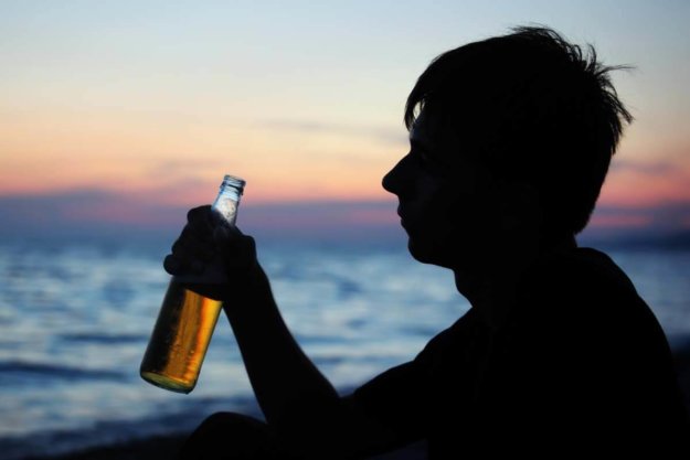 a teenage boy drinking a beer on the beach signs of teen alcoholism