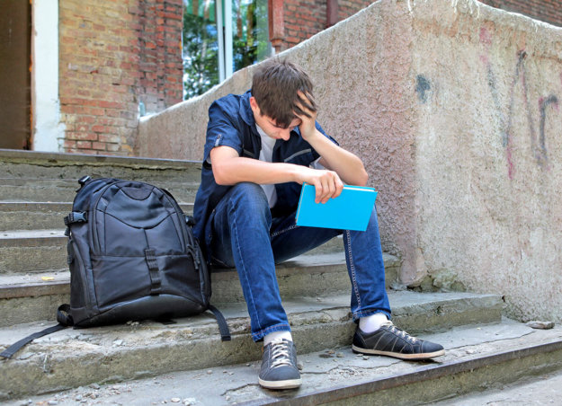 teen sitting on school steps with hand pressed to forehead because of stress affecting teenagers