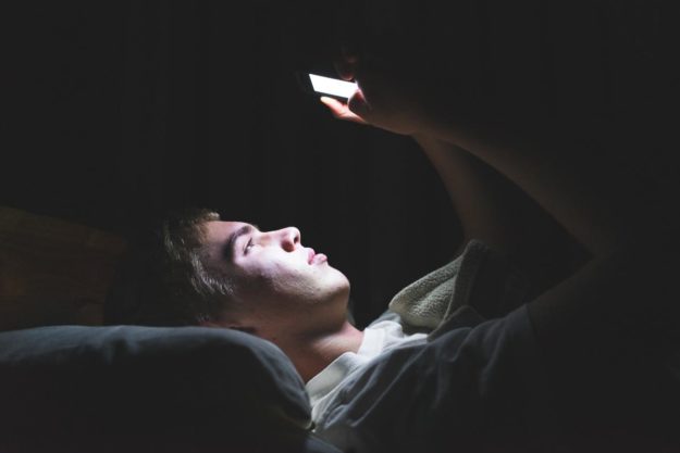 a teenager laying in bed on his phone learning about the common signs of drug abuse in teens