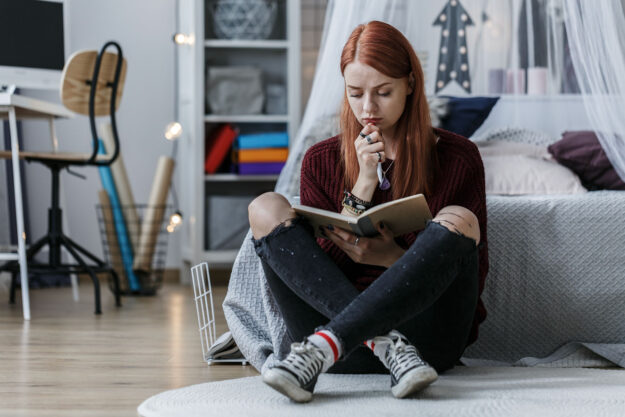 an angsty moody teen sits alone in her bedroom reading